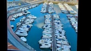 A marina with numerous boats docked in a circular layout, a clear blue sky, and a distant view of a large ship and a mountainous landscape. - Ertzilla apartament - Sea view. (Bermeo)