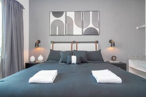 Ett modernt hotellrum med en stor säng, två sängbord, ett litet bord, en vägglampa och en tavla ovanför sängen.