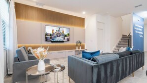 Ein modernes Wohnzimmer mit grauem Sofa, einem flachbildfernseher an der Wand und einer dekorativen Wandverkleidung.