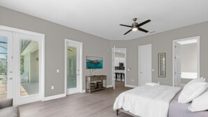 A bedroom with a bed, a ceiling fan, and a view of the backyard through glass doors.
