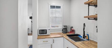 A compact kitchen with white cabinets, a microwave, a coffee maker, and a sink.