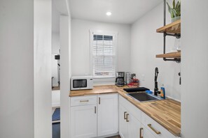 A compact kitchen with white cabinets, a microwave, a coffee maker, and a sink.
