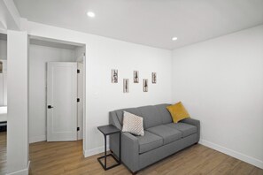 A modern living room with a grey sofa, a small black side table, and a wooden floor.