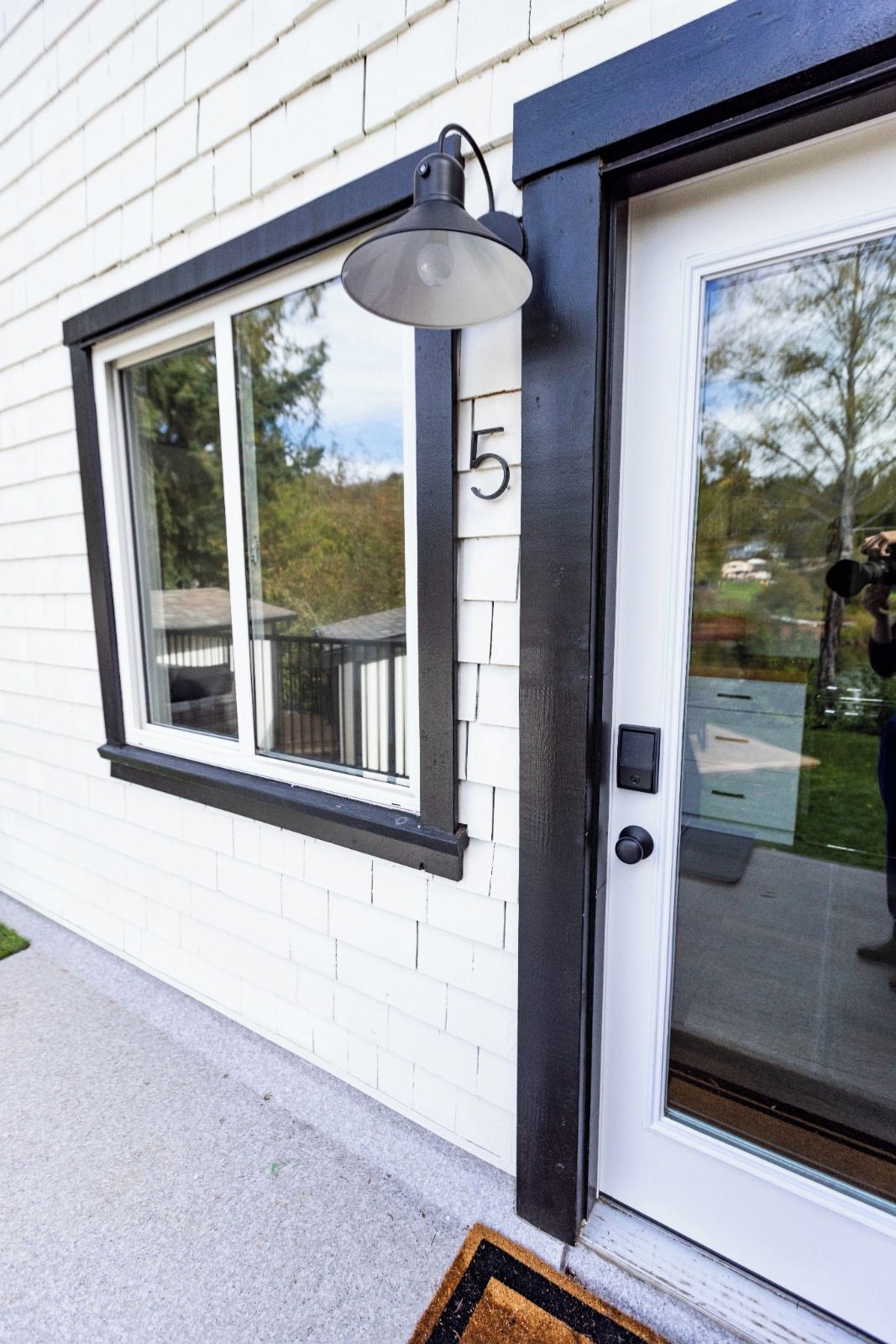 Une maison à l’extérieur blanc, avec une fenêtre à cadre noir et une porte sur laquelle est inscrit le chiffre « 5 ».