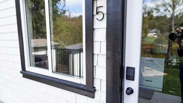 Une maison à l’extérieur blanc, avec une fenêtre à cadre noir et une porte sur laquelle est inscrit le chiffre « 5 ».