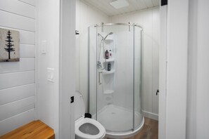 A modern bathroom with a glass-enclosed shower, a toilet, and a wooden floor. - Charming Riverside Suite | Kitchenette, BBQ, Dock (Lake Cowichan)