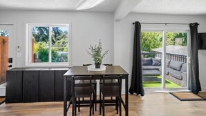 Une cuisine moderne avec un coin repas, une grande fenêtre et une porte-fenêtre coulissante donnant sur une terrasse extérieure.