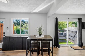 A modern kitchen with a dining area, a large window, and a sliding glass door leading to an outdoor patio. - Charming Riverside Suite | Kitchenette, BBQ, Dock (Lake Cowichan)