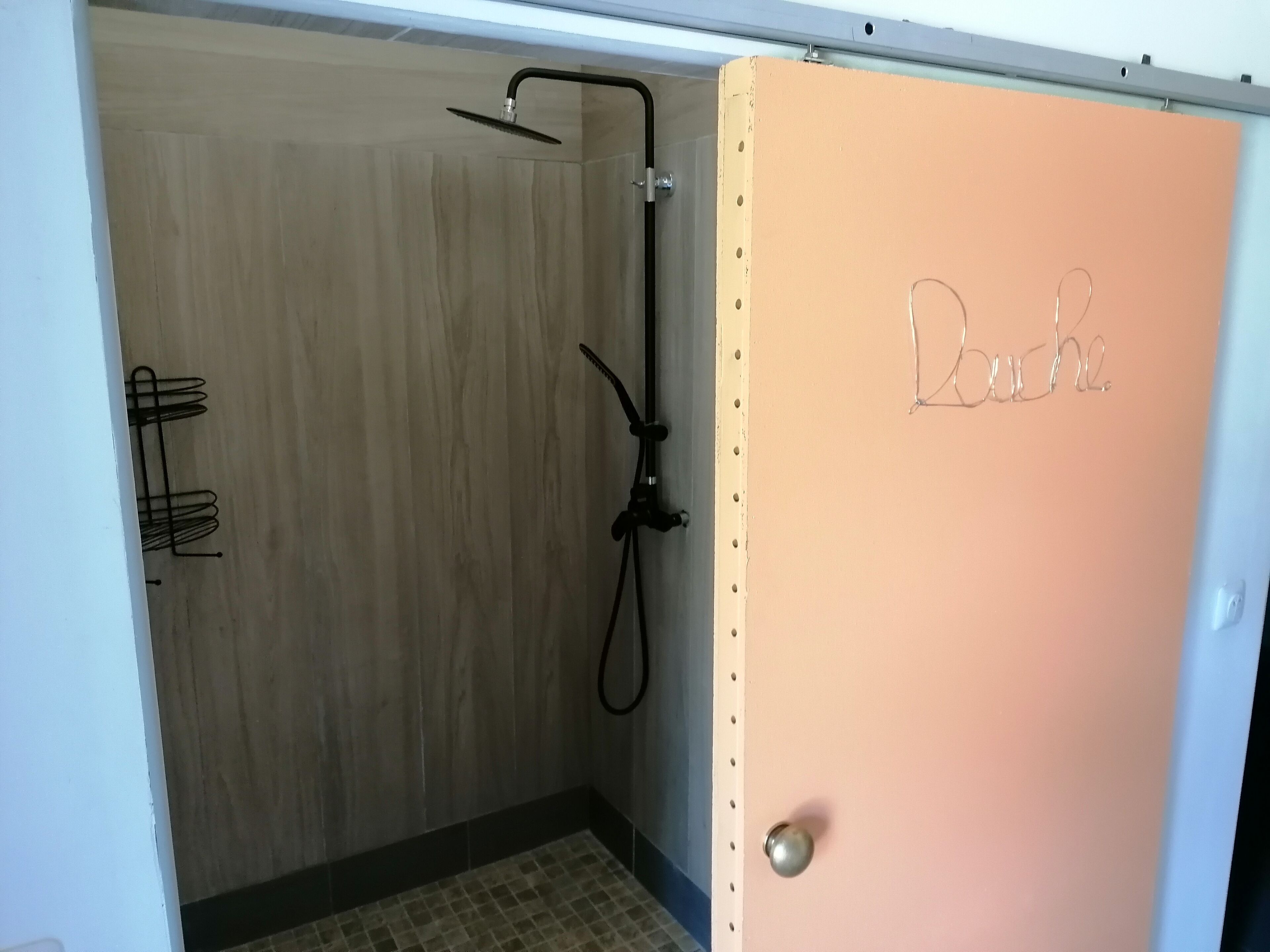 A shower area with a wooden wall, a showerhead, and a door labeled "Bouche".
