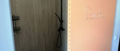 Un espace douche avec un mur en bois, une pomme de douche et une porte portant l’inscription « Bouche ».