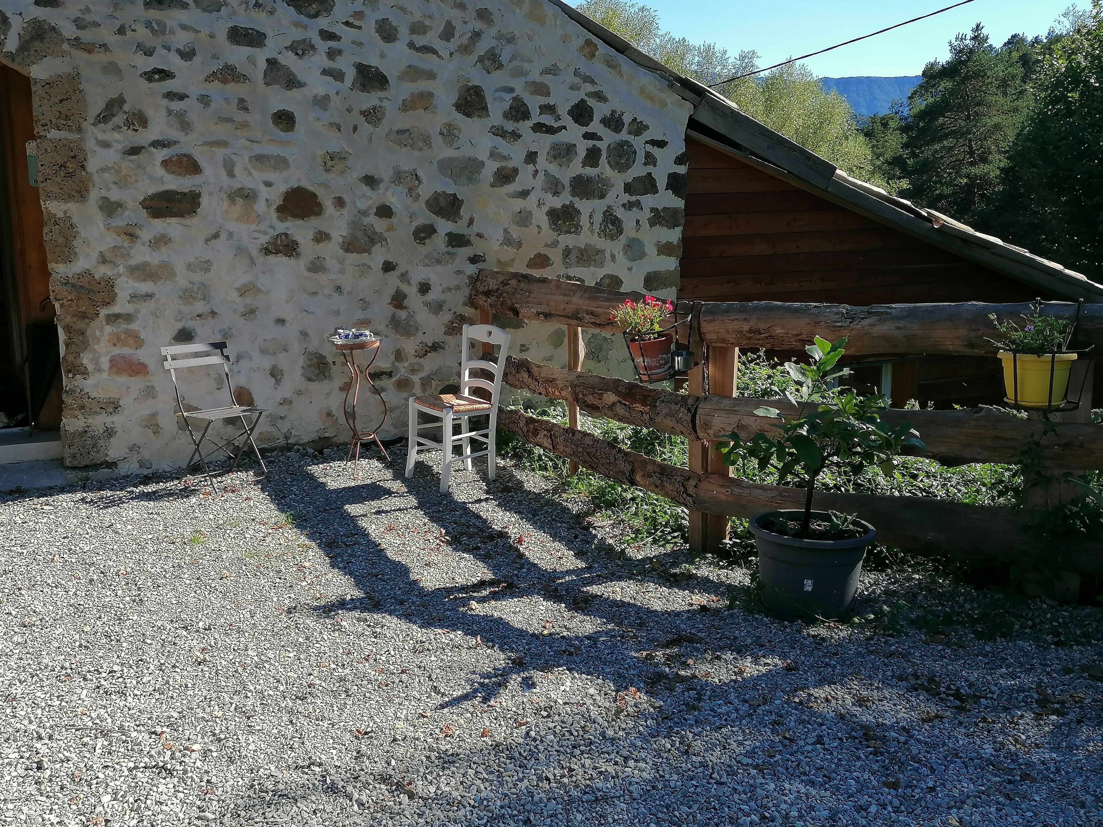 A rustic stone building with a wooden porch, a gravel driveway, and a wooden fence.