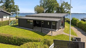 Ein modernes Haus mit flachem Dach, großen Fenstern und Blick auf das Wasser.