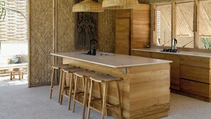 Uma cozinha de madeira com ilha central, banquetas e duas luminárias pendentes.