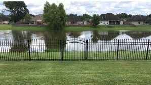 Une zone herbeuse clôturée, avec un plan d’eau et des maisons en arrière-plan.