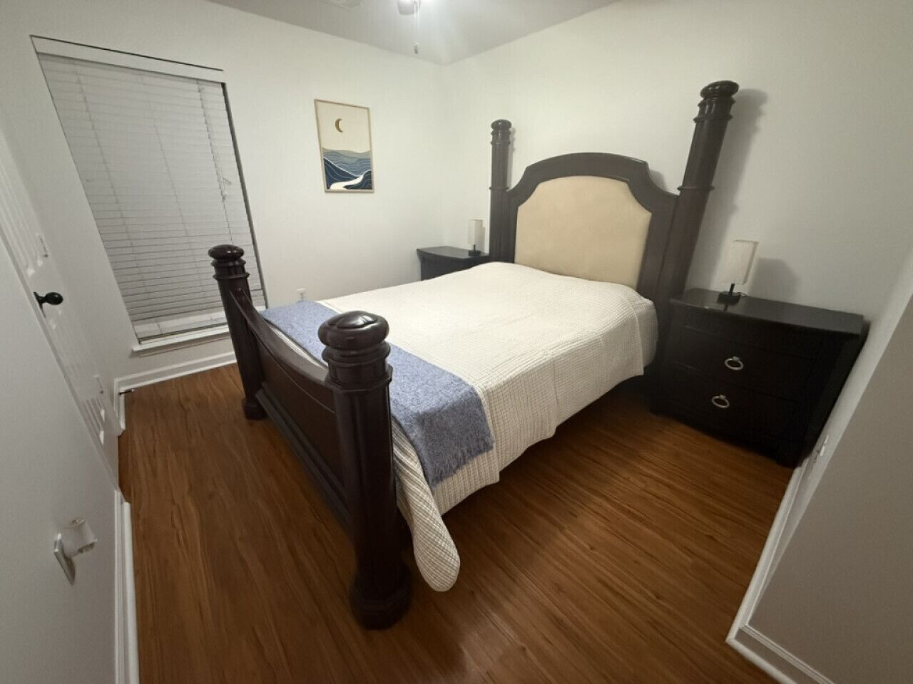 Un dormitorio con una cama de madera, una mesita de noche, un aparador y una ventana con persianas.