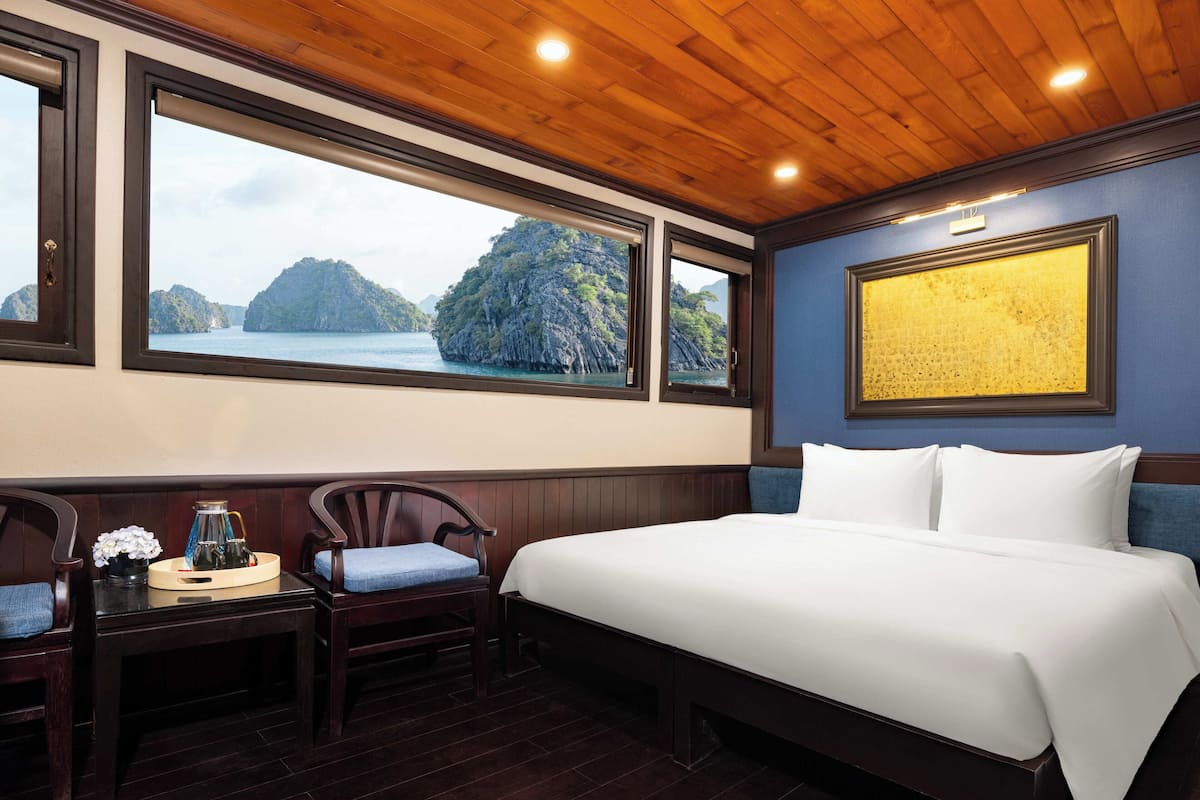 A hotel room with a large bed, wooden ceiling, and a view of a mountainous landscape through large windows.