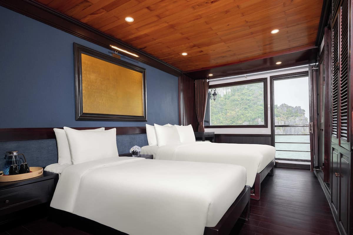 A hotel room with two beds, a large window with a view of greenery, and a wooden ceiling.