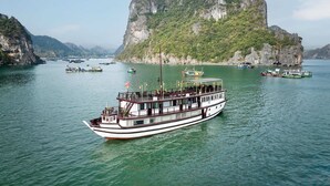 A boat with a dining area and a flag on top, surrounded by calm water and rocky cliffs. - Garden Bay Legend 2 cruise (Bai Chay)