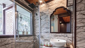A bathroom with a glass-enclosed shower, a marble wall, a large mirror, and a white sink. - Garden Bay Legend 2 cruise (Bai Chay)