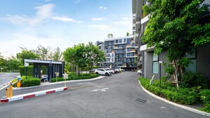 A modern building with multiple floors, a parking area with several cars, and a small kiosk. - Laguna Skypark B2512 (Choeng Thale)