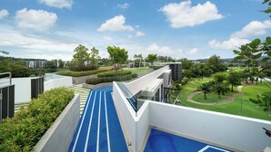 A modern building with a blue pathway leading to a rooftop area with a view of a park and distant buildings. - Laguna Skypark B2512 (Choeng Thale)