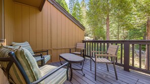 A wooden deck with outdoor furniture, including a sofa and chairs, overlooking a forested area.