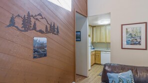 A wooden wall with a mountain silhouette and a Shaver Lake sign, a framed painting, and a kitchen with wooden cabinets and a white refrigerator.