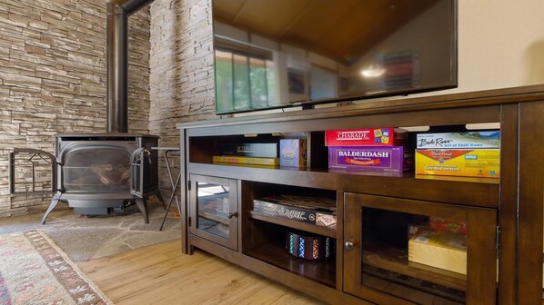 A living room with a stone wall, a fireplace, a television, and a shelf with board games.