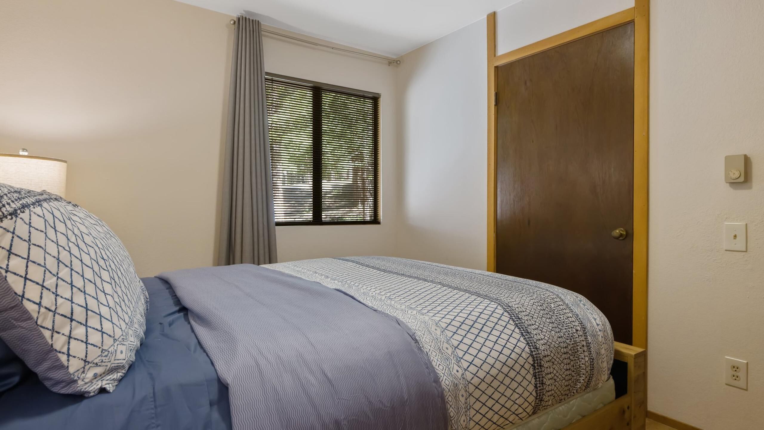 Ein Schlafzimmer mit Bett, Fenster mit Rollläden, Tür und einer Steckdose.