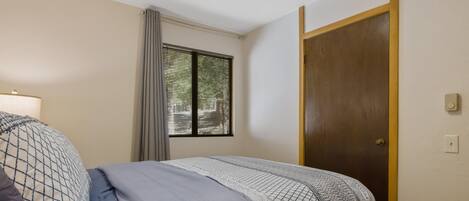 Ein Schlafzimmer mit Bett, Fenster mit Rollläden, Tür und einer Steckdose.