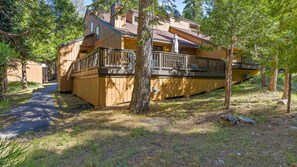 A wooden cabin with a deck and a covered outdoor seating area, surrounded by trees.