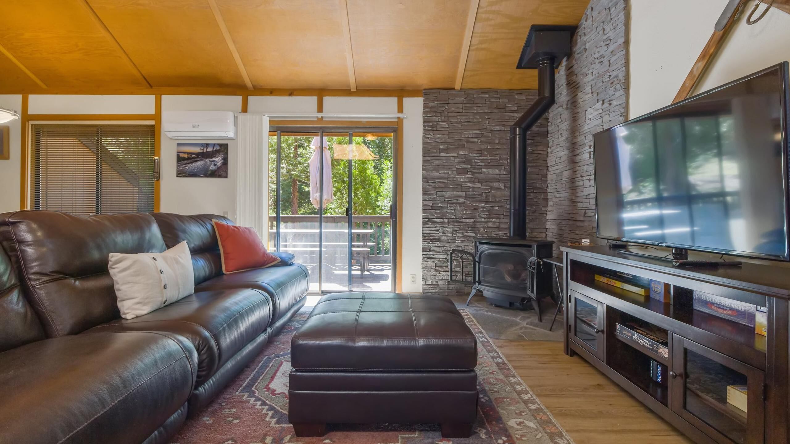 A modern living room with a leather sofa, ottoman, and a flat-screen TV on a wooden cabinet.