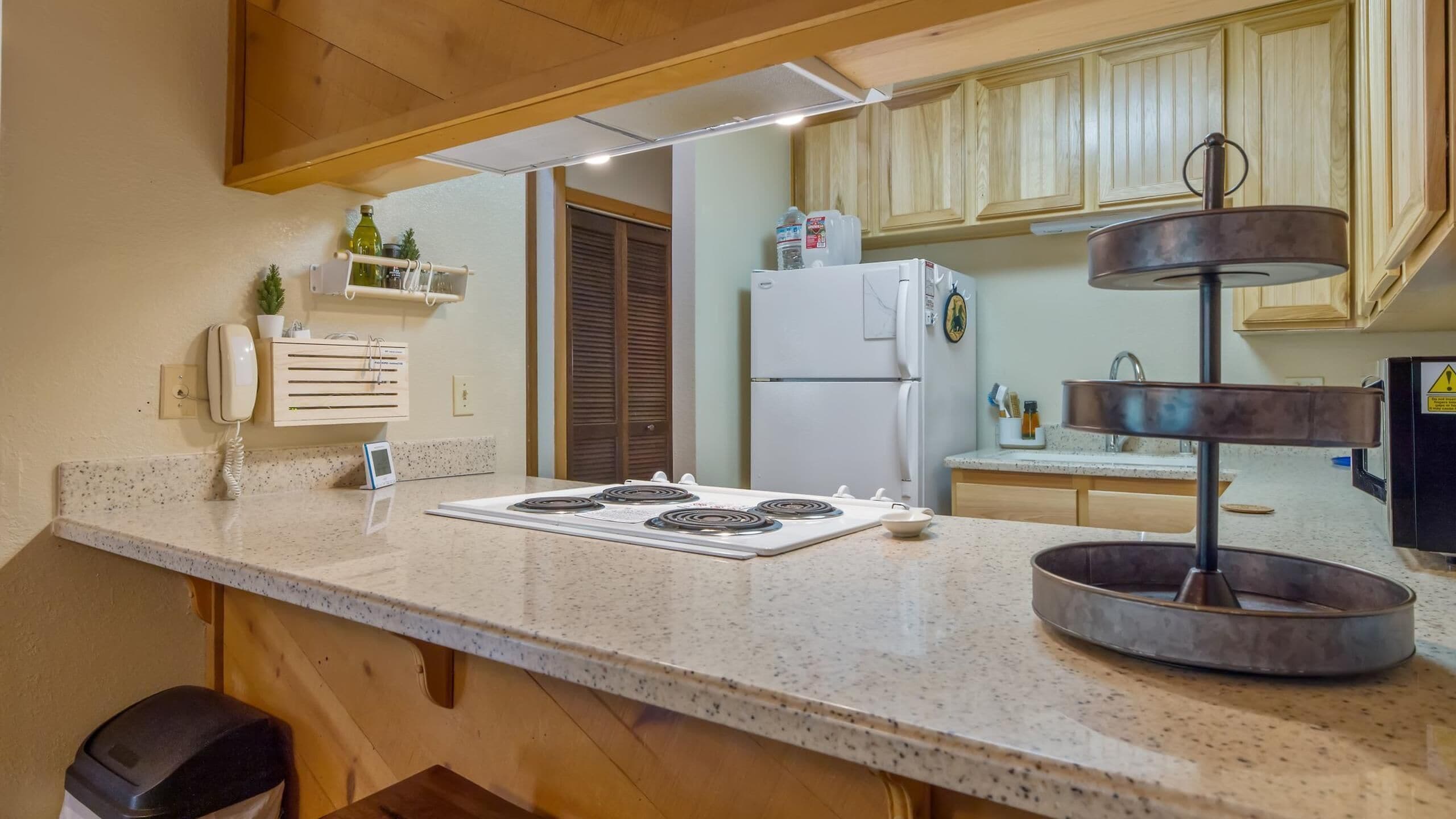 A kitchen with a granite countertop, a stove, a refrigerator, wooden cabinets, a phone, and a water dispenser.