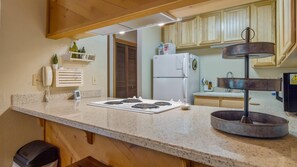A kitchen with a granite countertop, a stove, a refrigerator, wooden cabinets, a phone, and a water dispenser.