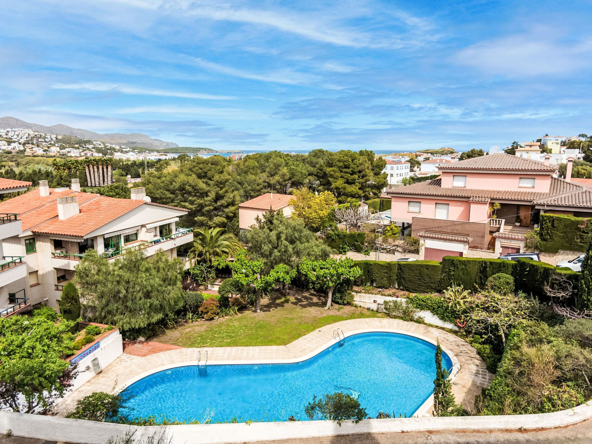 A residential area with a swimming pool surrounded by lush greenery and houses with red-tiled roofs.