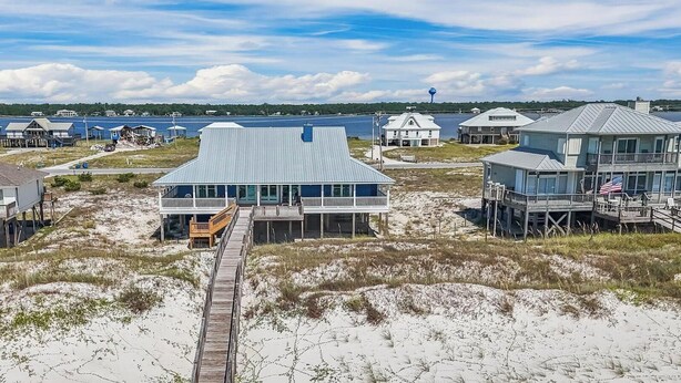 Une propriété située sur la côte, avec un bâtiment principal relié à d’autres constructions par une promenade en bois, le tout entouré de maisons de plage.