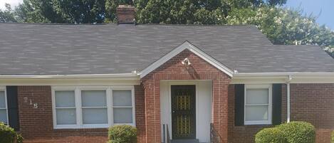A single-story brick house with a front door, a small porch, and a well-maintained lawn.