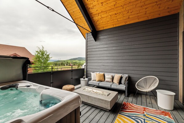 Een terras met een jacuzzi, een bank met kussens, een stoel en een vuurkorf.