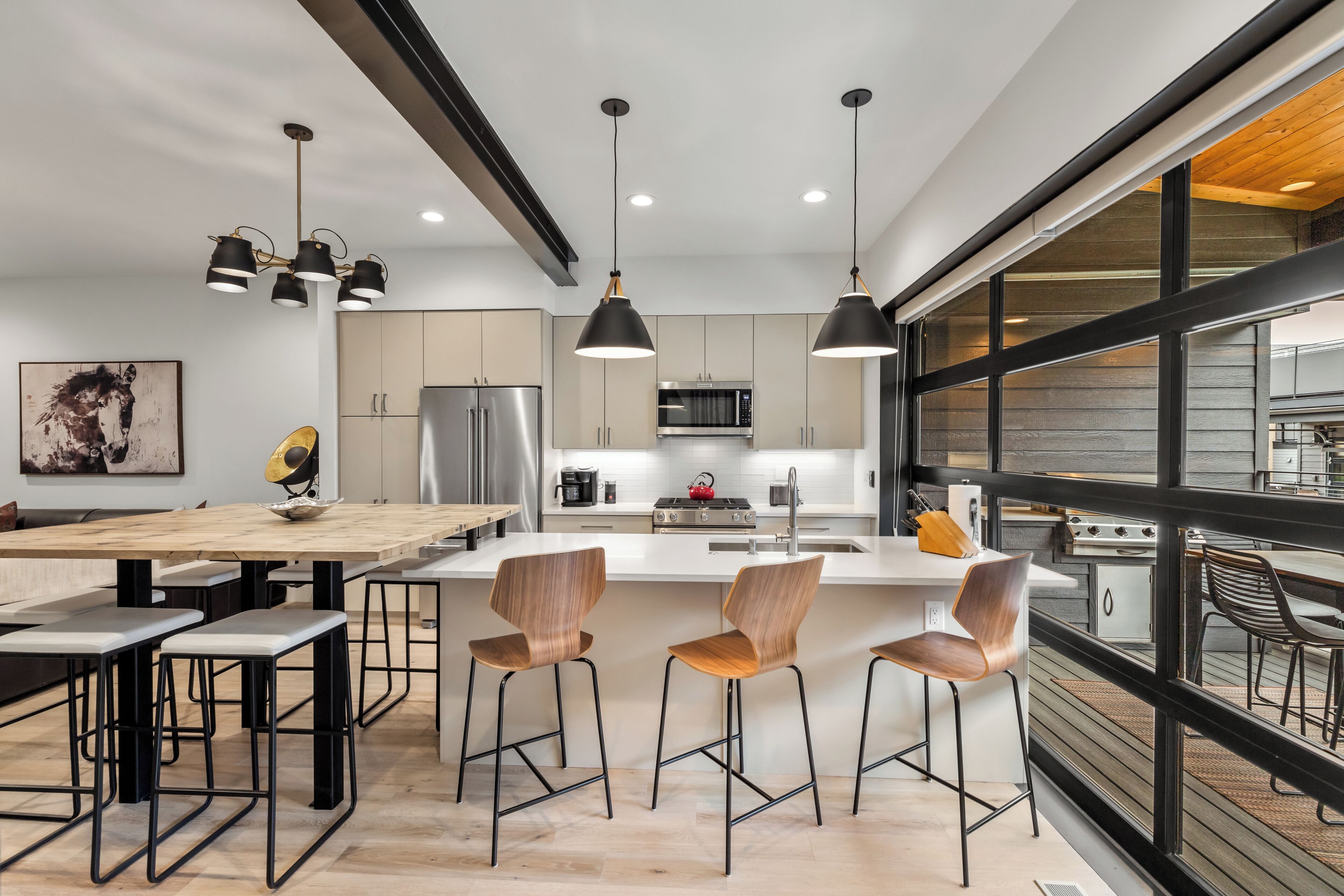 A modern kitchen with a central island, pendant lighting, and a view of the outdoor deck.