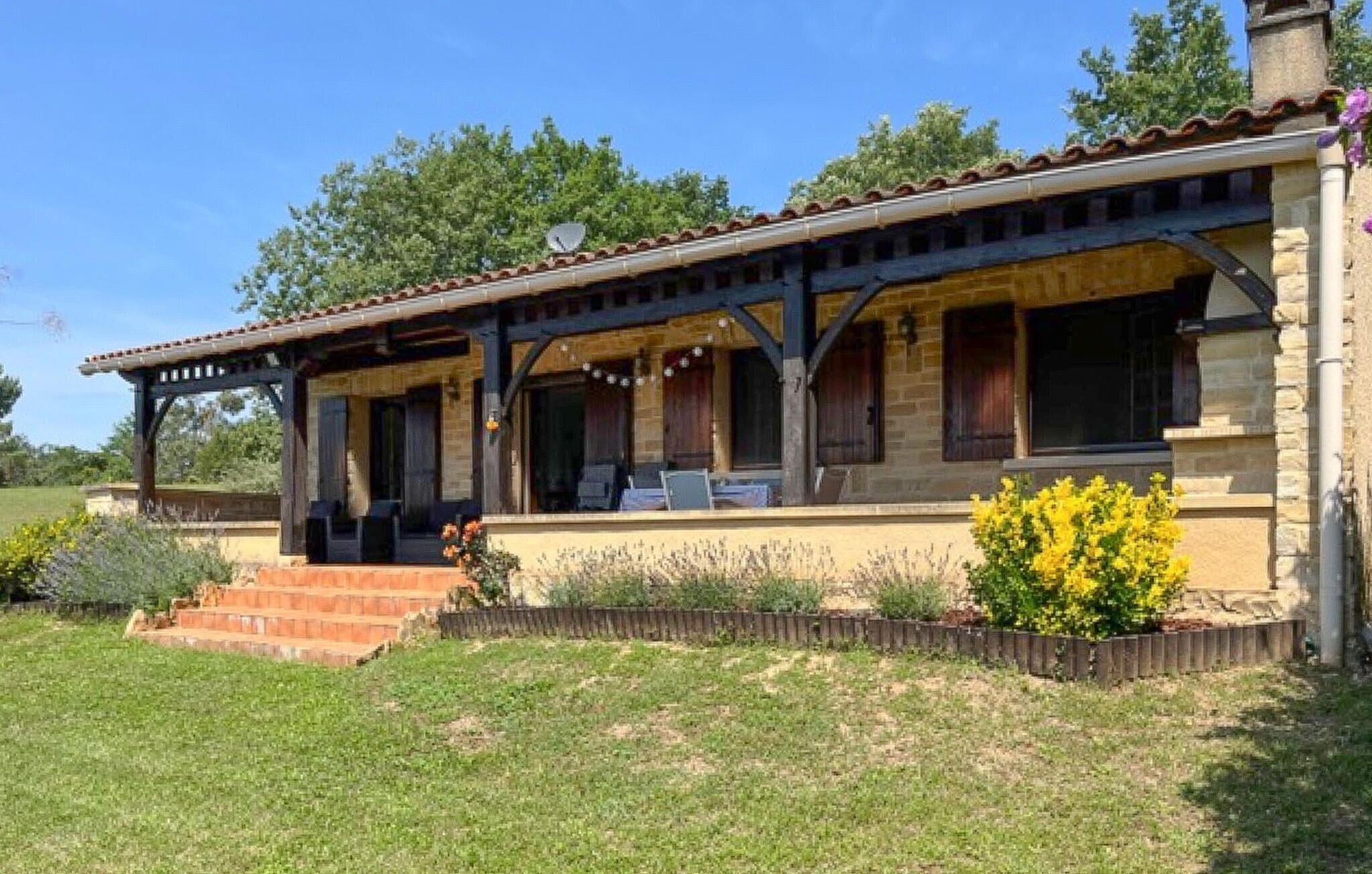 A two-story stone building with a covered patio and a small garden area with yellow flowers.