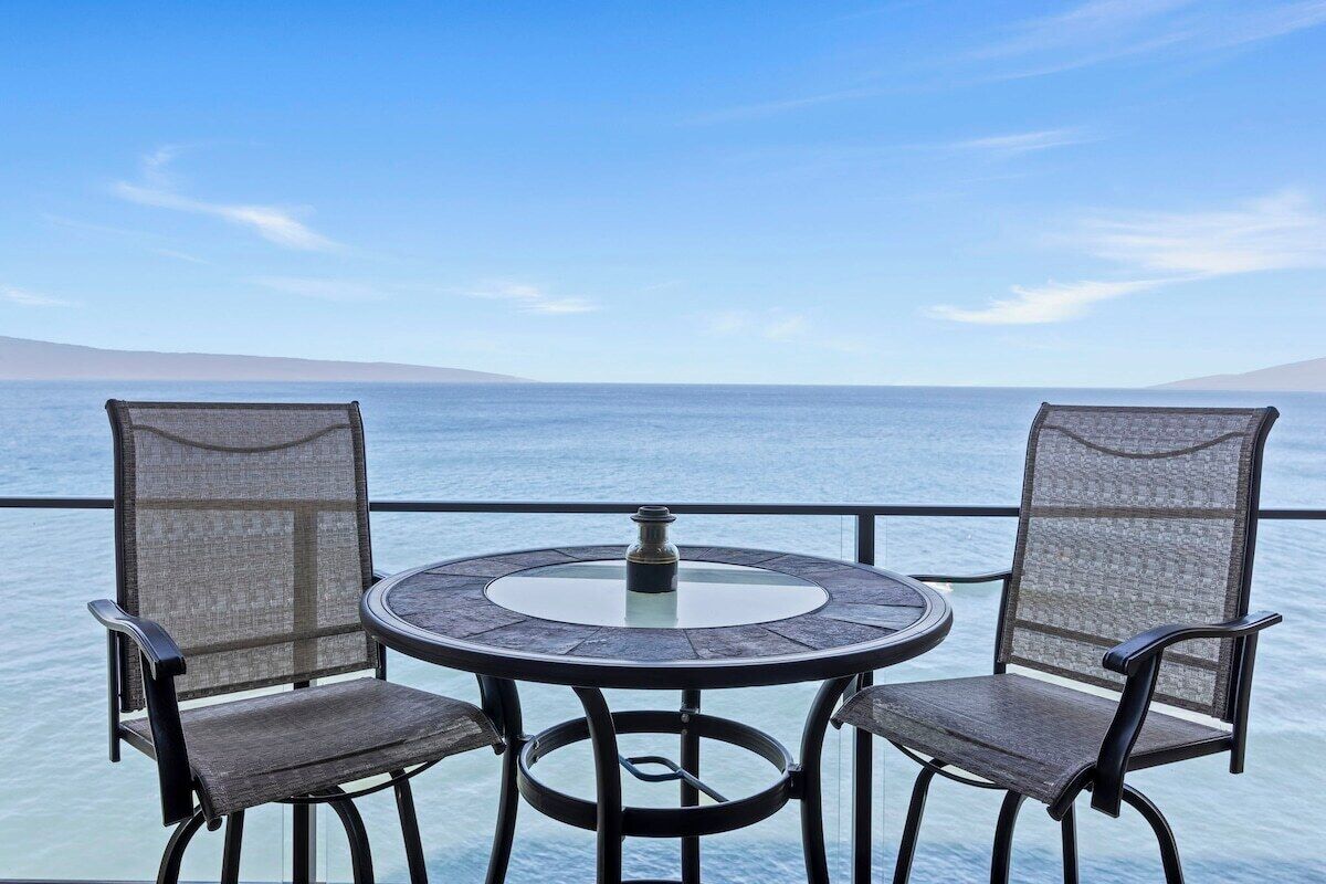 Une table ronde avec deux chaises, placée sur un balcon donnant sur une étendue d’eau.