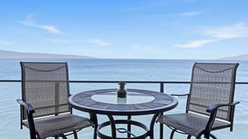 Une table ronde avec deux chaises, placée sur un balcon donnant sur une étendue d’eau.