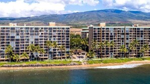 A beachfront hotel with multiple high-rise buildings, a beach, and a mountain in the background. - Perch - Oceanfront Tranquility: 1BR Condo w/ Views (Lahaina)