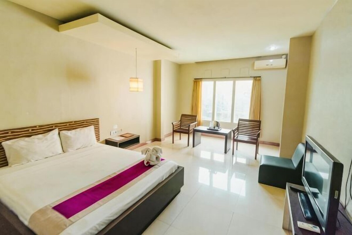 A hotel room with a large bed, a desk, a chair, and a TV.