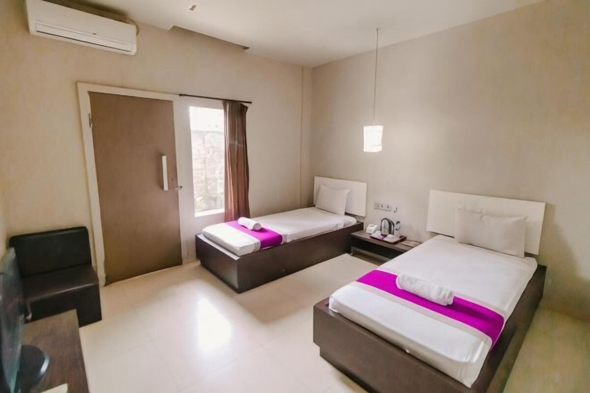 A hotel room with two beds, a desk, a chair, a wardrobe, and a window.