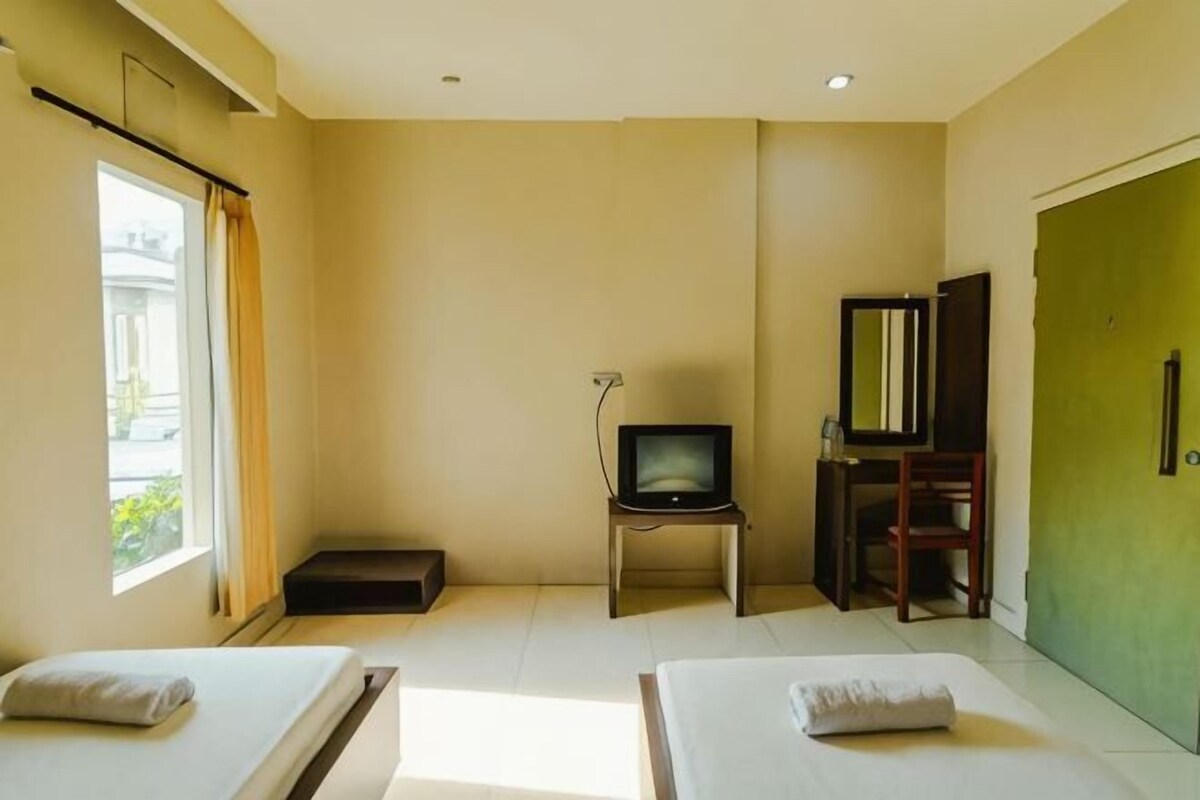 A hotel room with two beds, a television, a desk, and a green door.