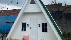 A white triangular house with a door, windows, and a small porch with a bench.