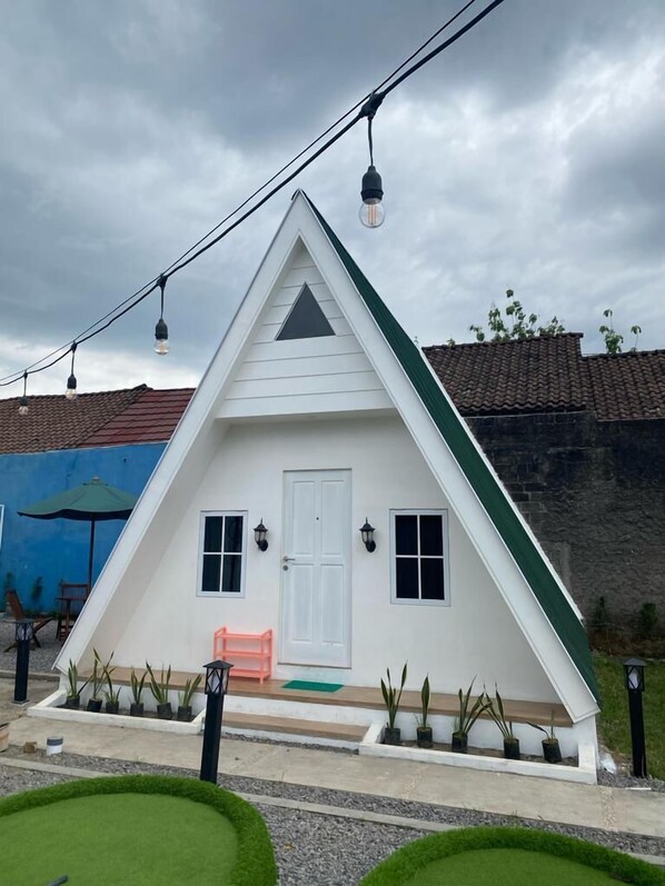 A white triangular house with a door, windows, and a small porch with a bench. - Tropical House and Mini Golf Yogyakarta (Depok)