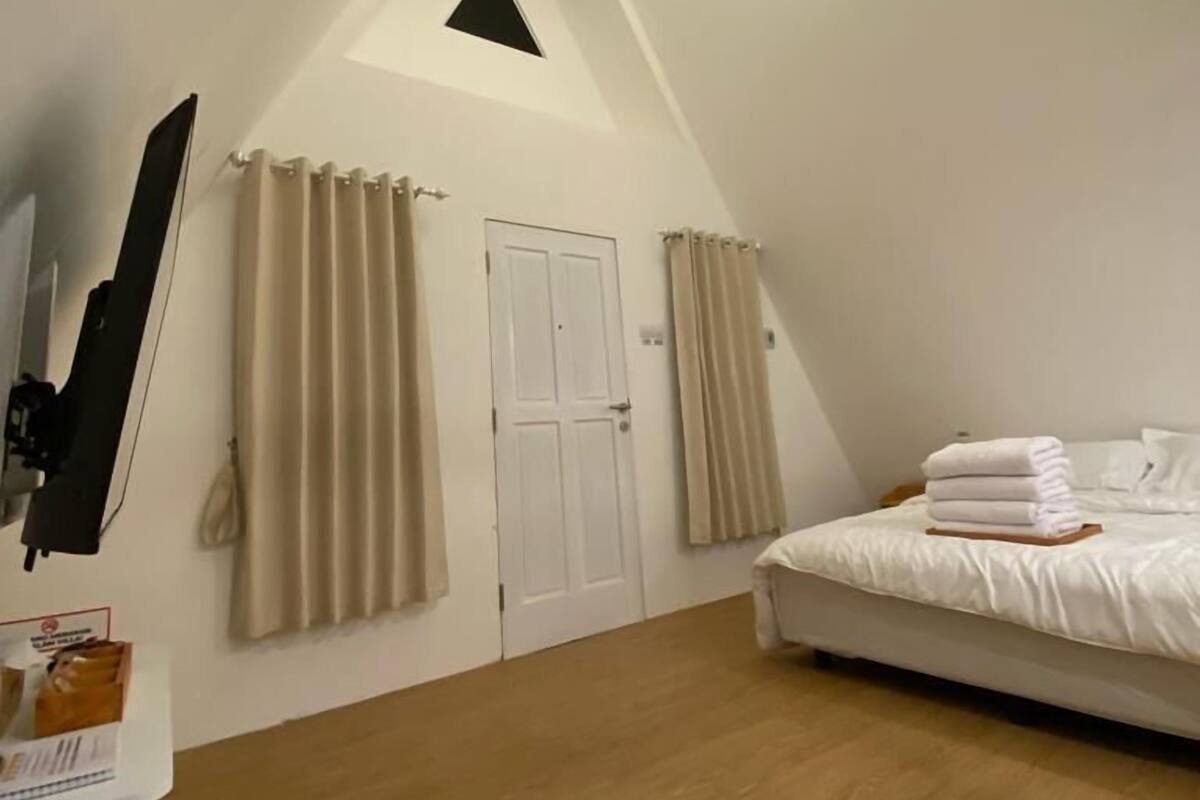 A bedroom with a sloped ceiling, a bed with white linens, a ceiling light fixture, and a door.
