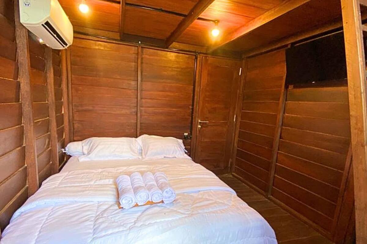 A wooden room with a bed, a ceiling fan, and an air conditioning unit.